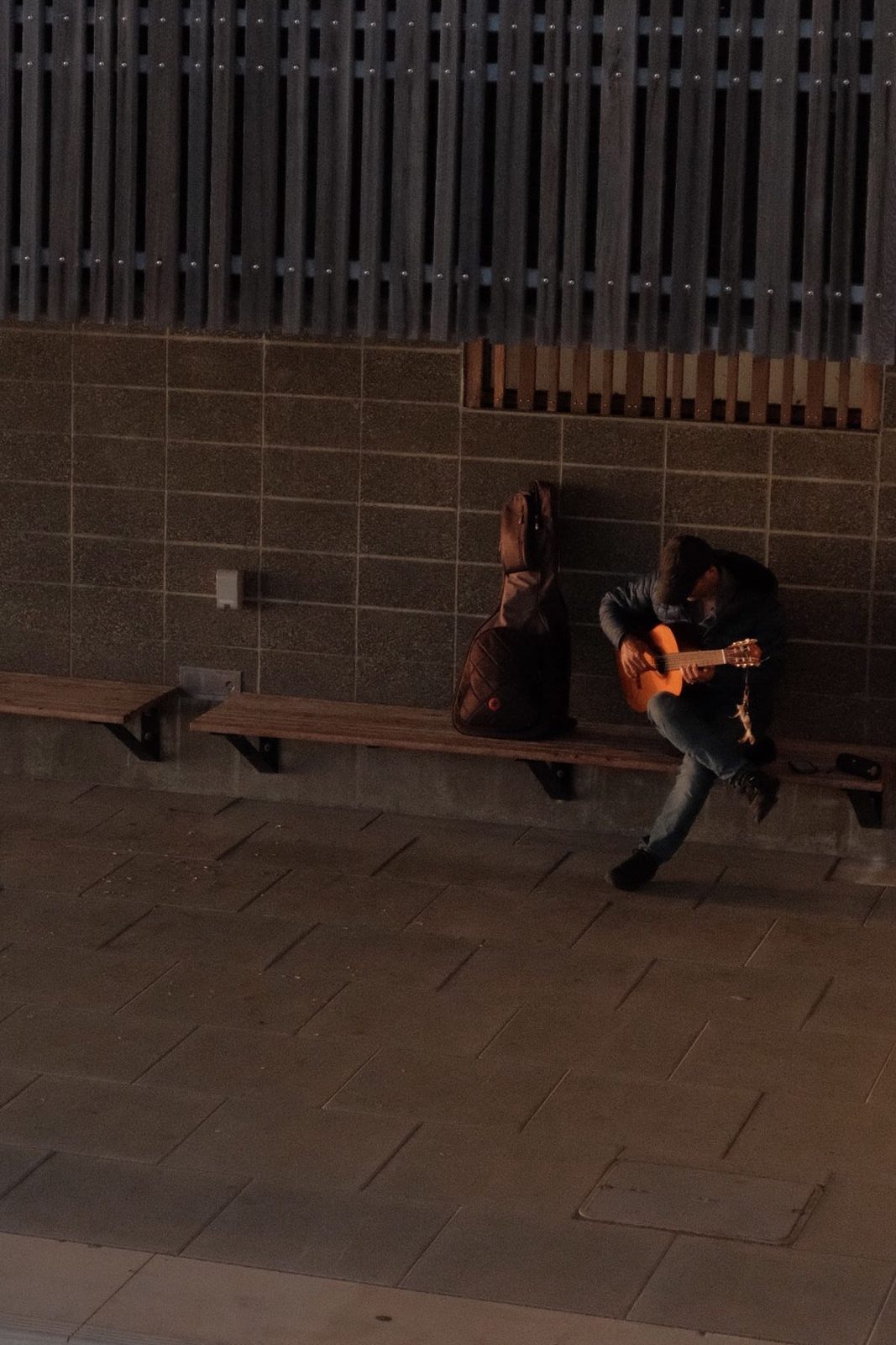 A guitarist playing alone on a bench at night, seen from above