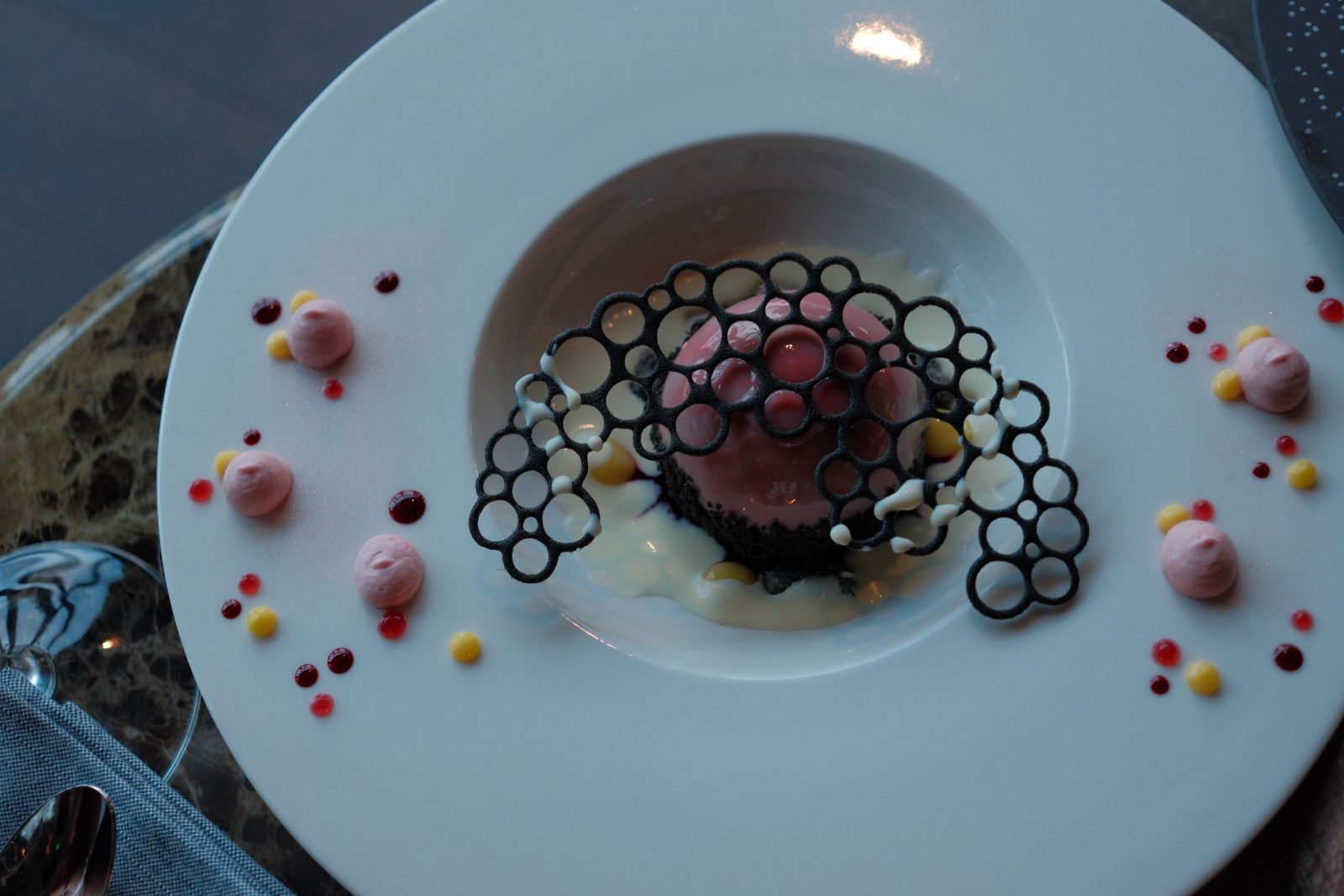 A plated dessert with a pink dome and a delicate chocolate lattice