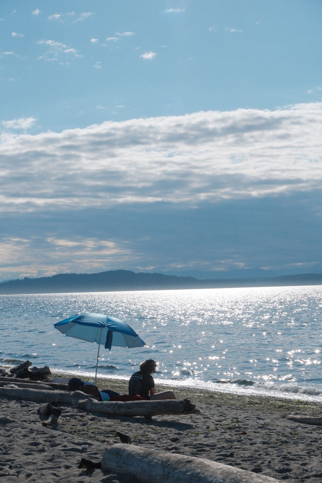 A blue beach umbrella on the sand as the sun sparkles on the water