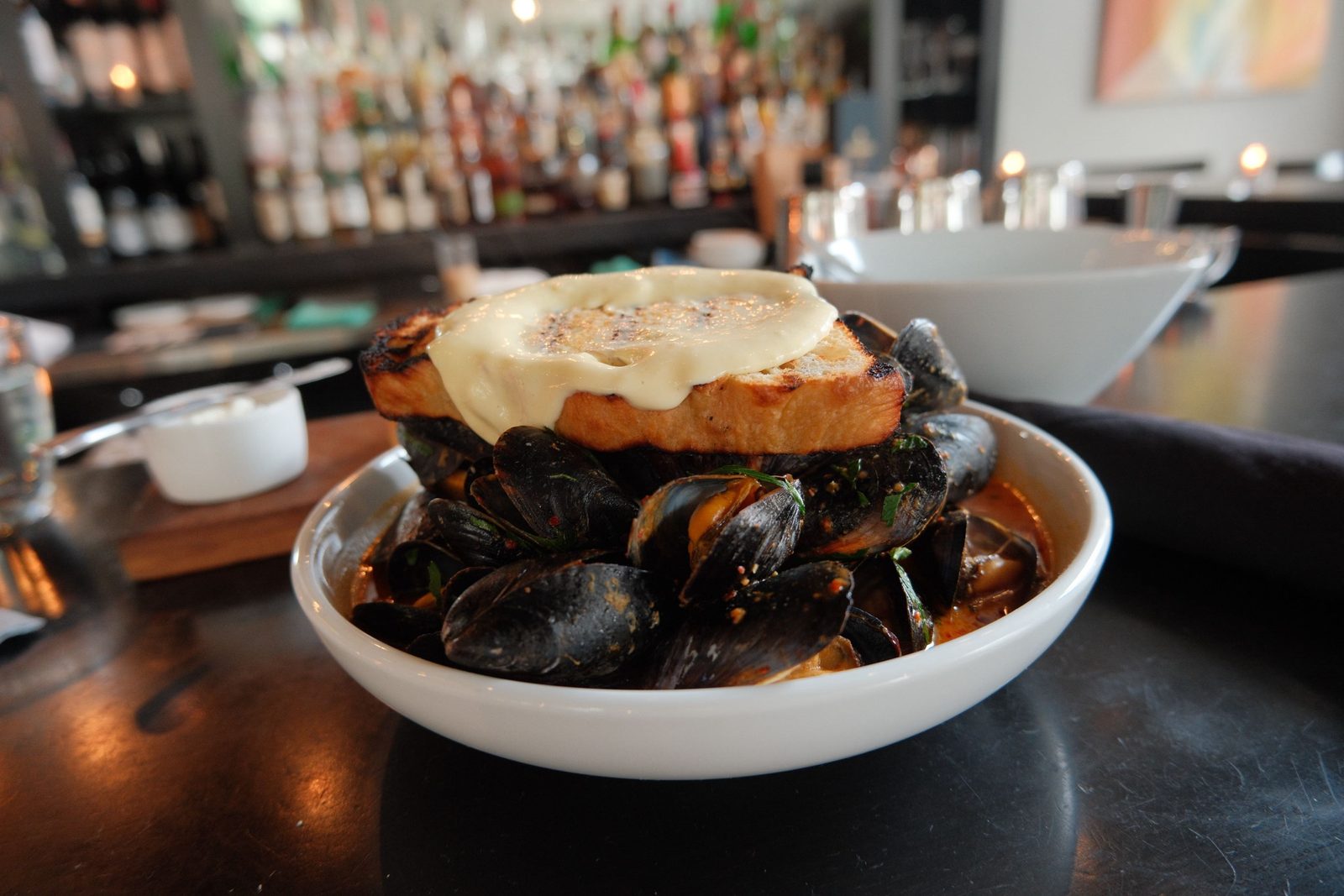 A bowl of mussels topped with a slab of grilled cheese toast