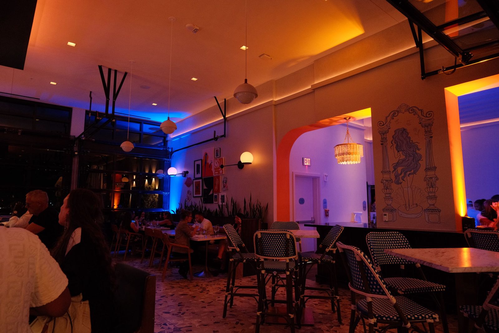 A restaurant washed in blue and orange light, with a painted mural