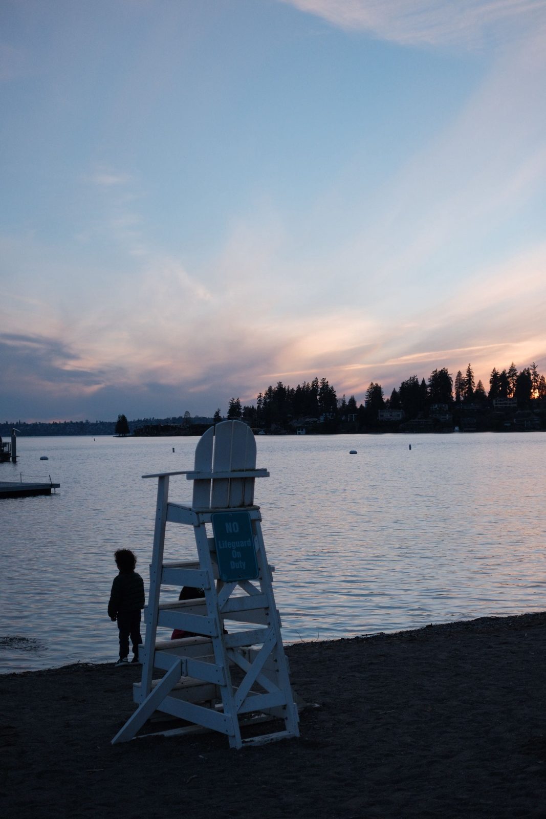 A lifeguard chair and a small child silhouetted on the beach at dusk