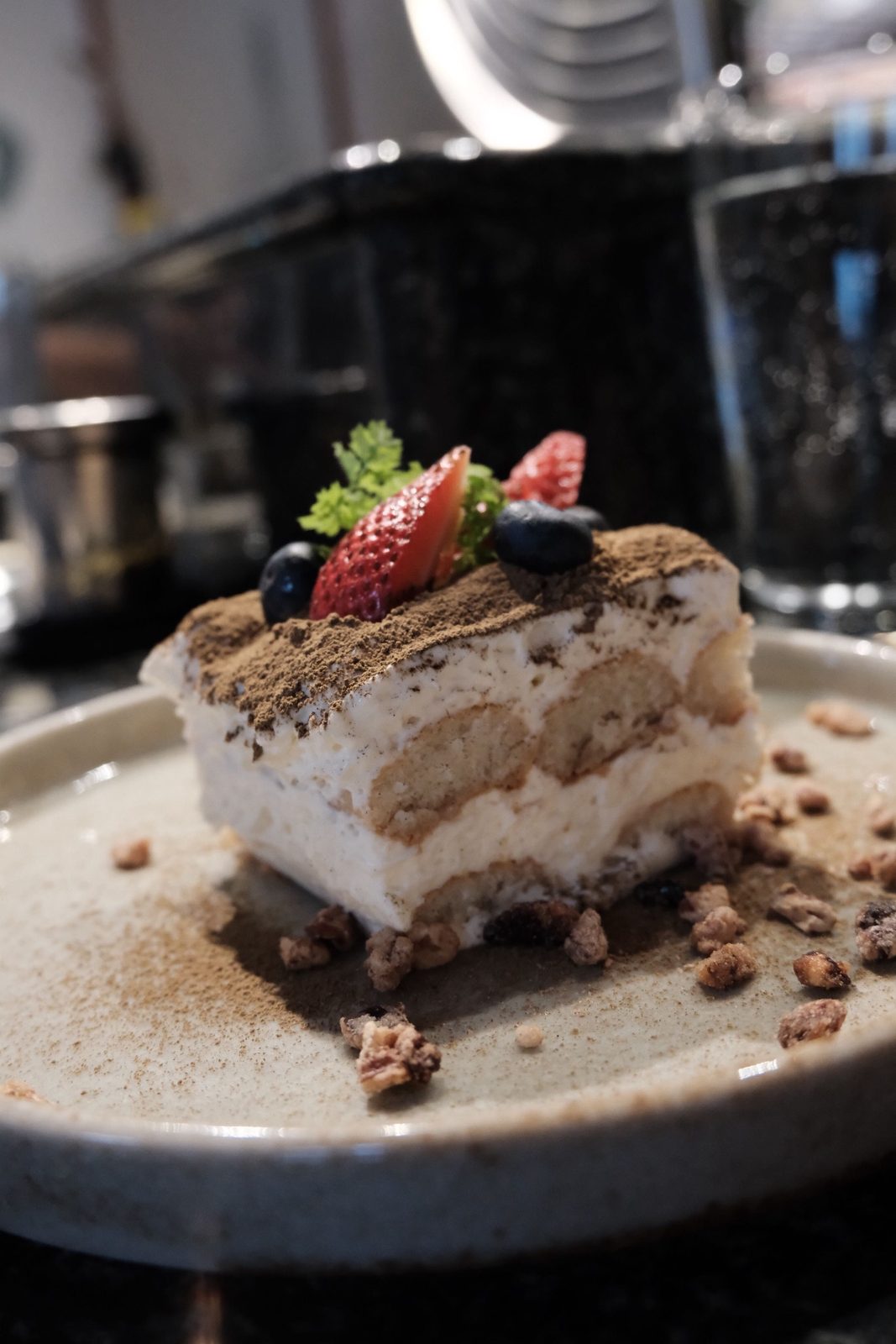A slice of tiramisu topped with strawberry and blueberries