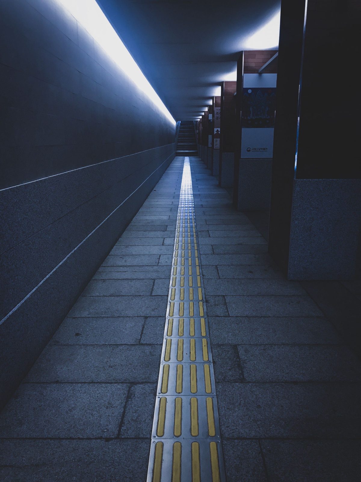 A quiet underground passage with a yellow tactile path leading to stairs