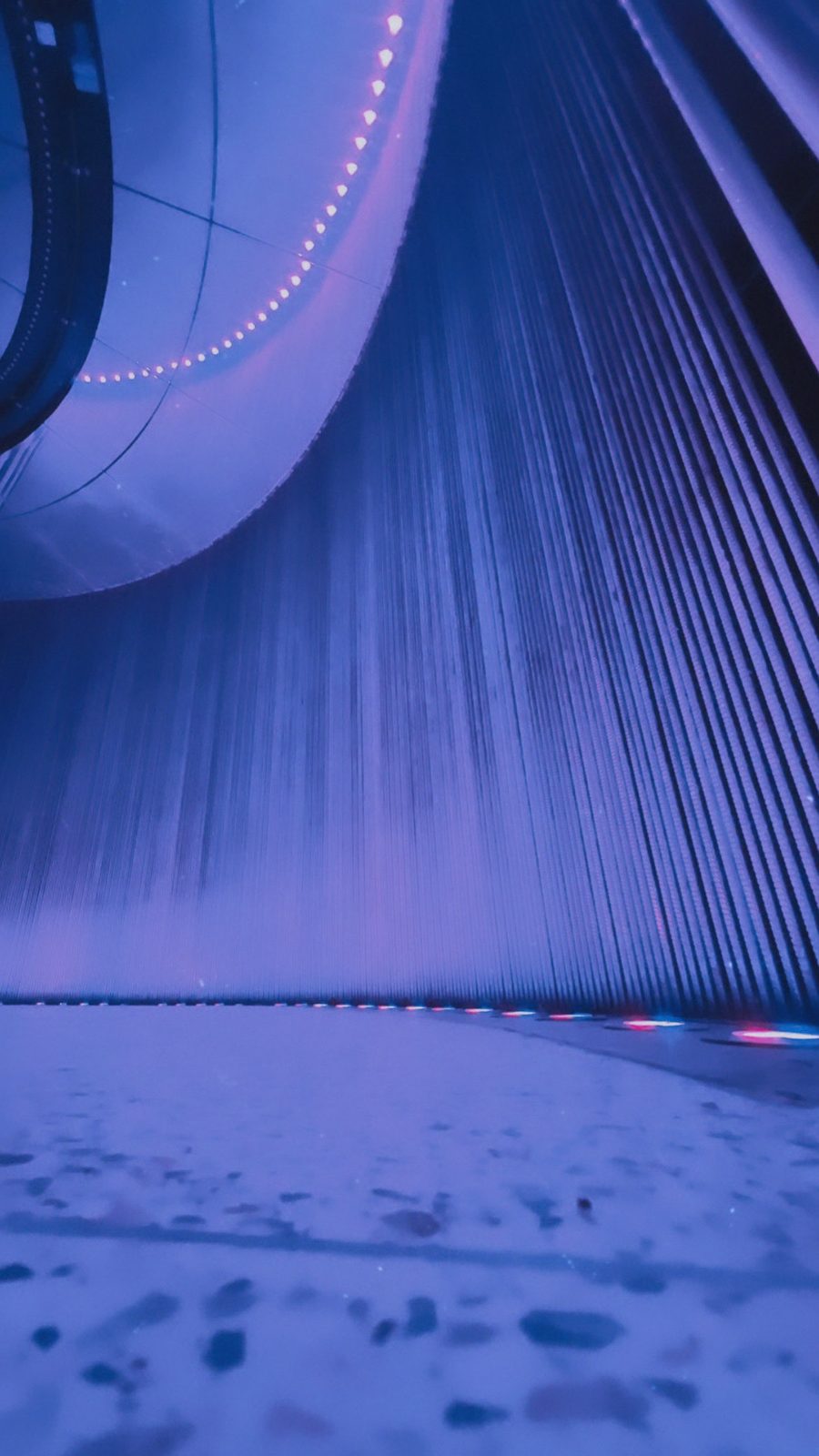 An abstract curve of architecture lit violet above a water feature
