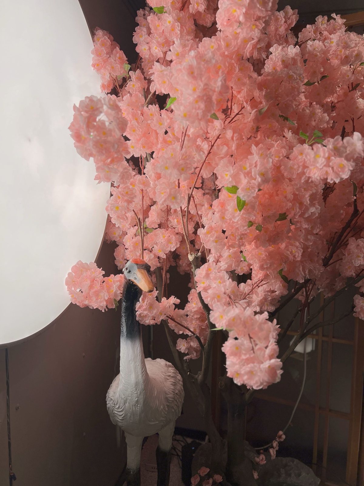 An indoor faux cherry-blossom tree beside a decorative crane