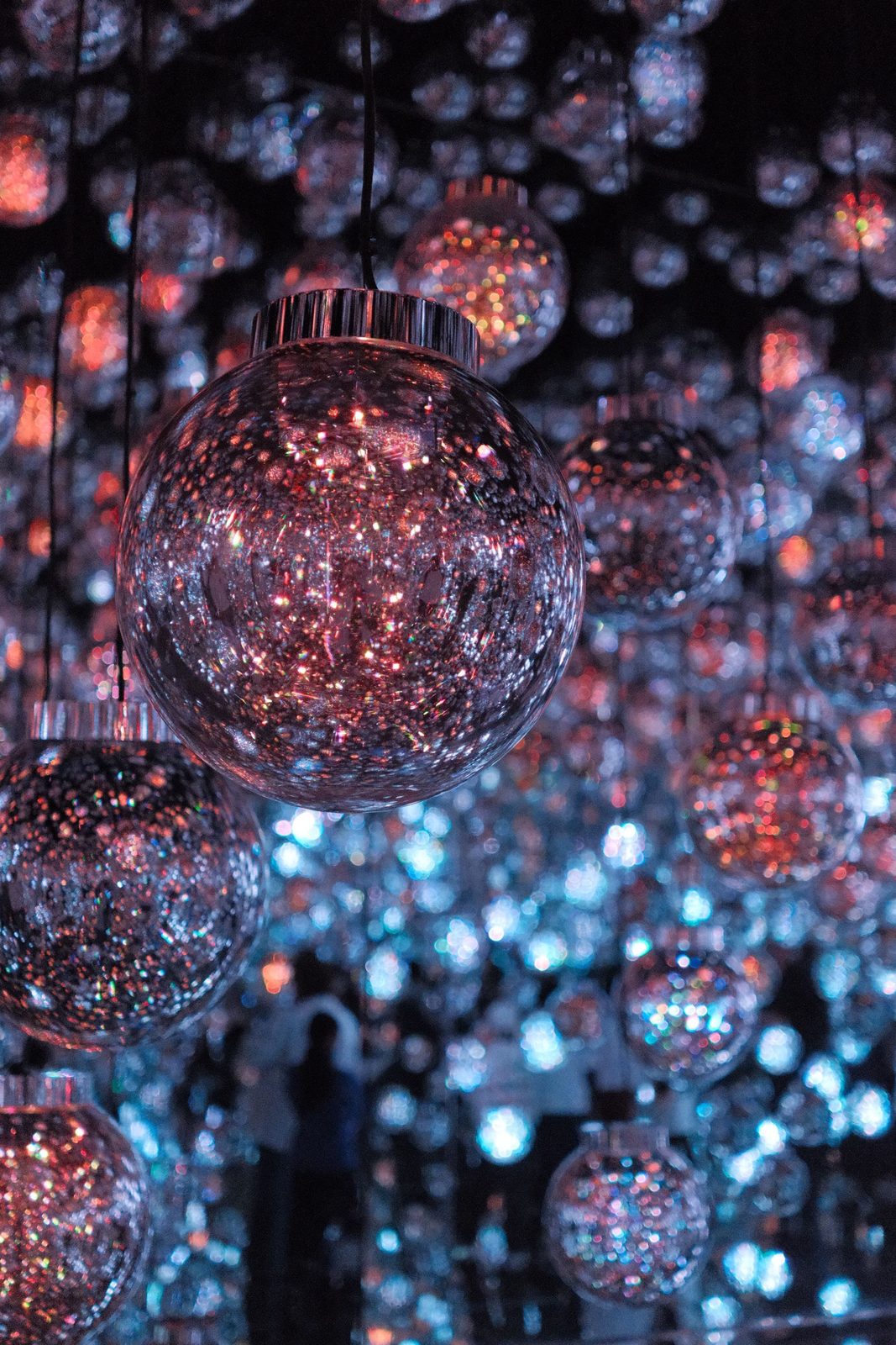 Pink and blue glitter glass ornament balls, people reflected below