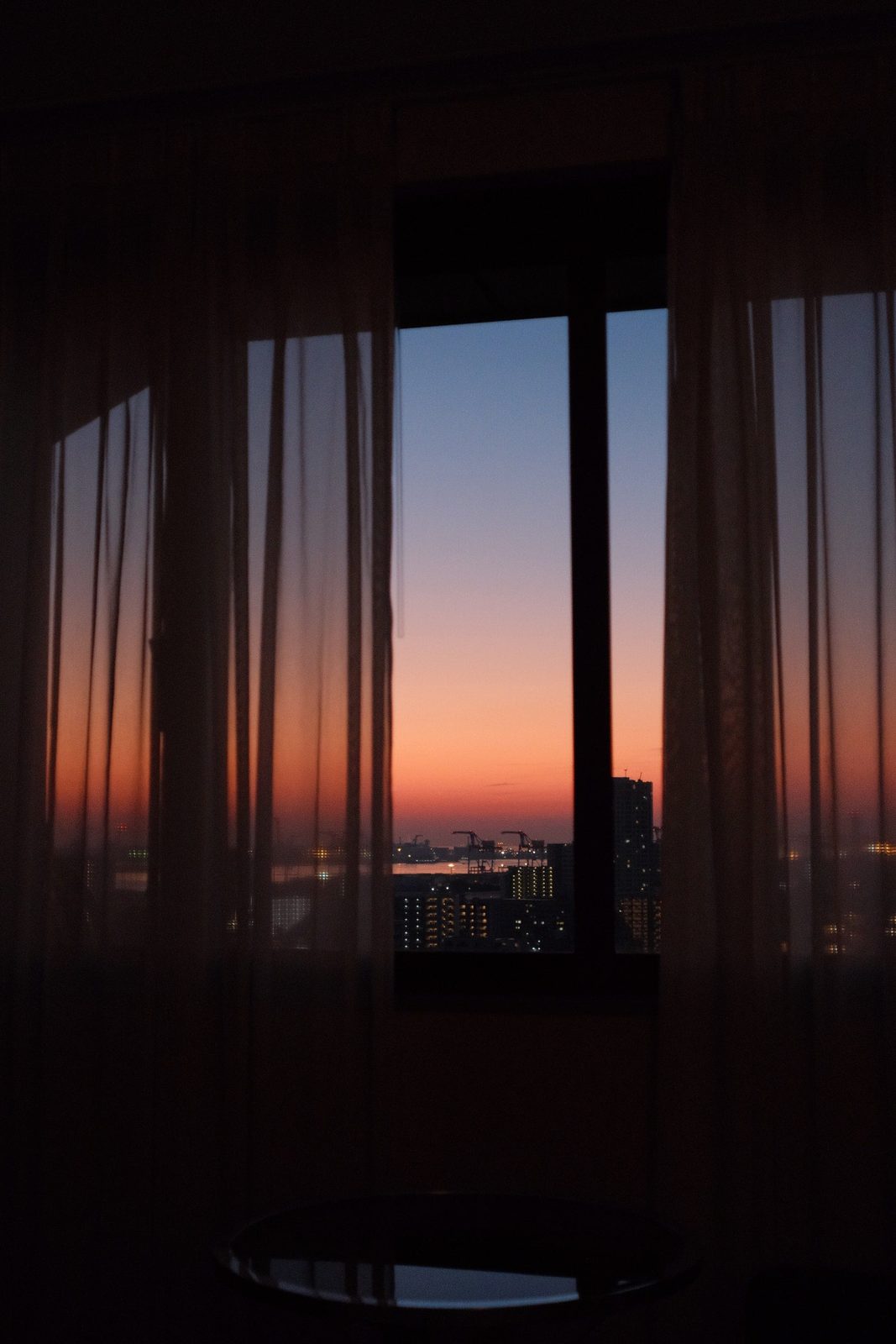 Sunset over the city seen through sheer hotel curtains