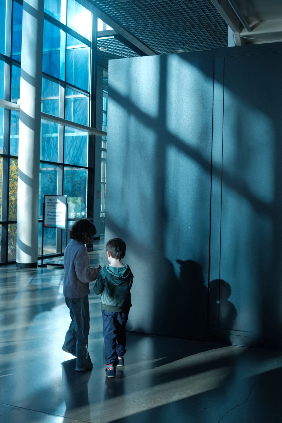 A woman and child in a blue-lit museum hallway, long shadows behind them
