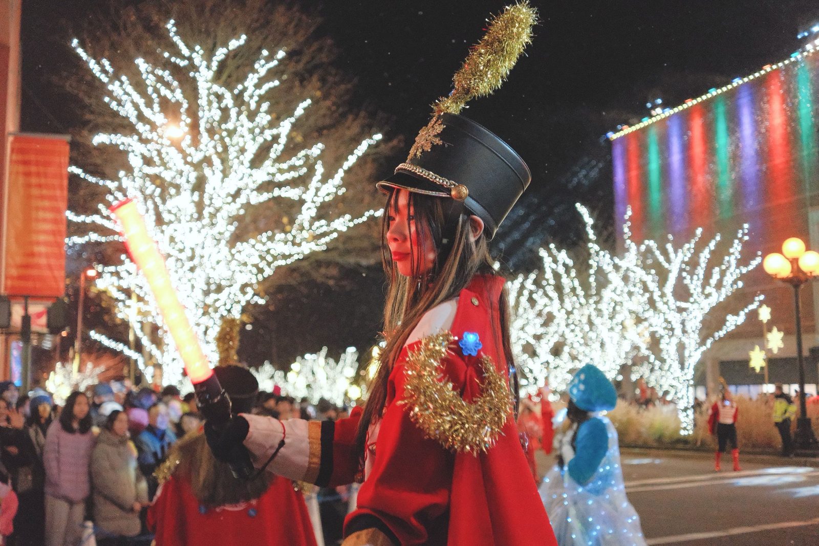 A festival performer in a red marching-band costume amid winter illuminations