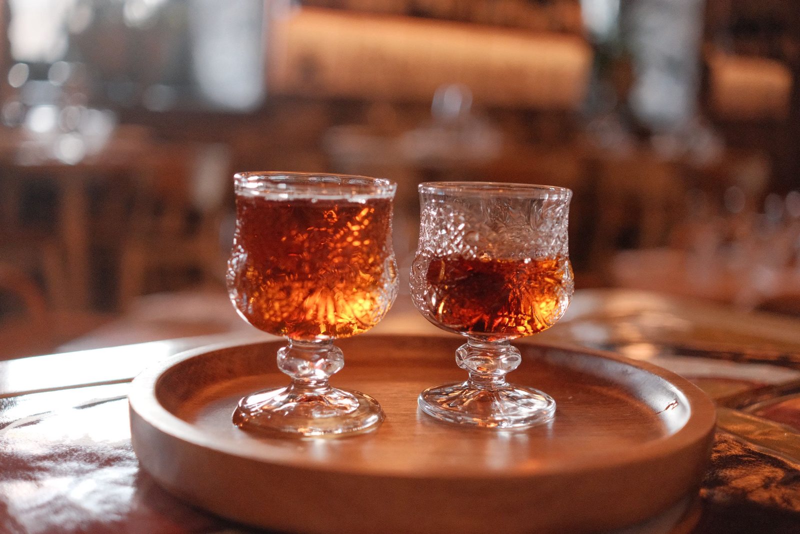 Two cut-glass goblets of amber liqueur on a wooden tray