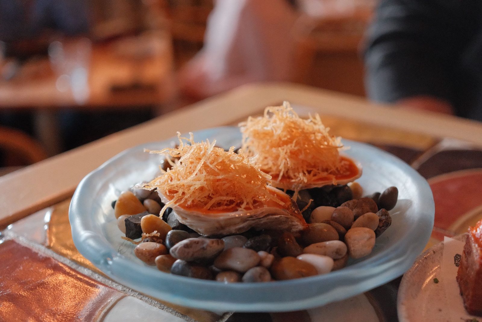 A plated oyster dish topped with crispy threads, served on river stones