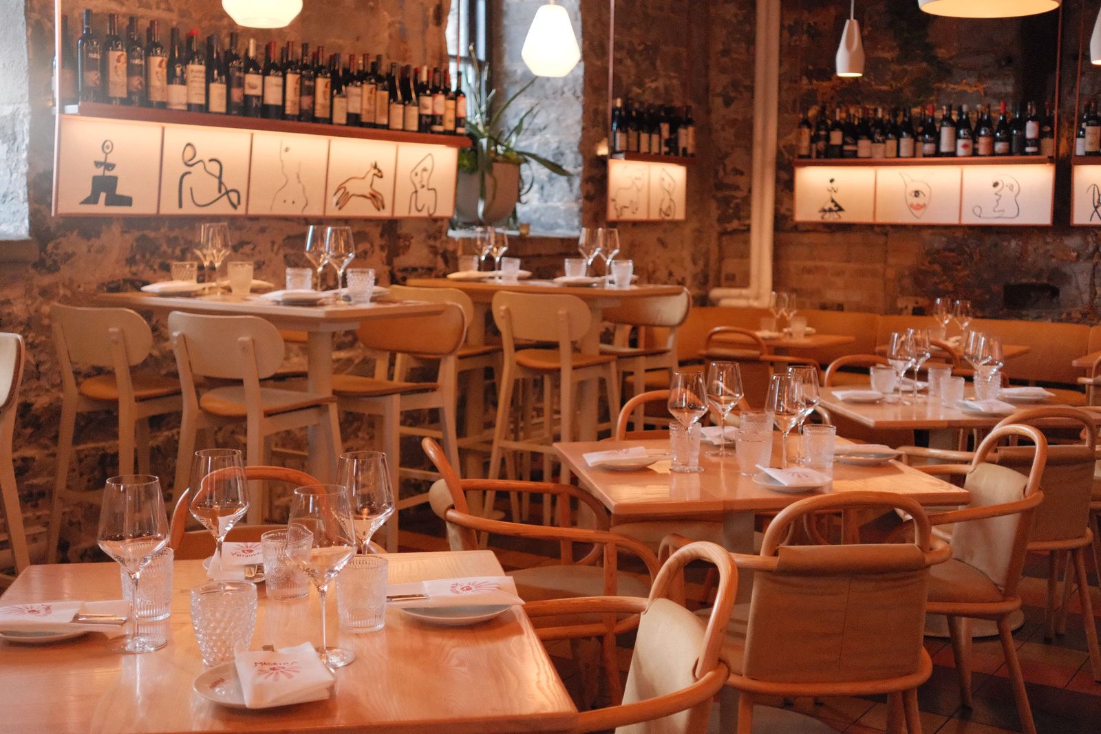 A warm wine bar with wooden chairs and bottle-lined walls