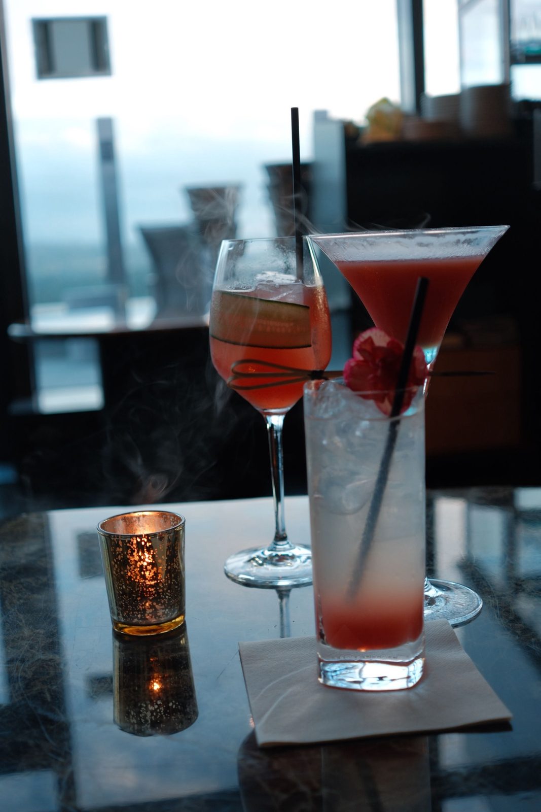 Three cocktails and a candle on a marble table with a city view