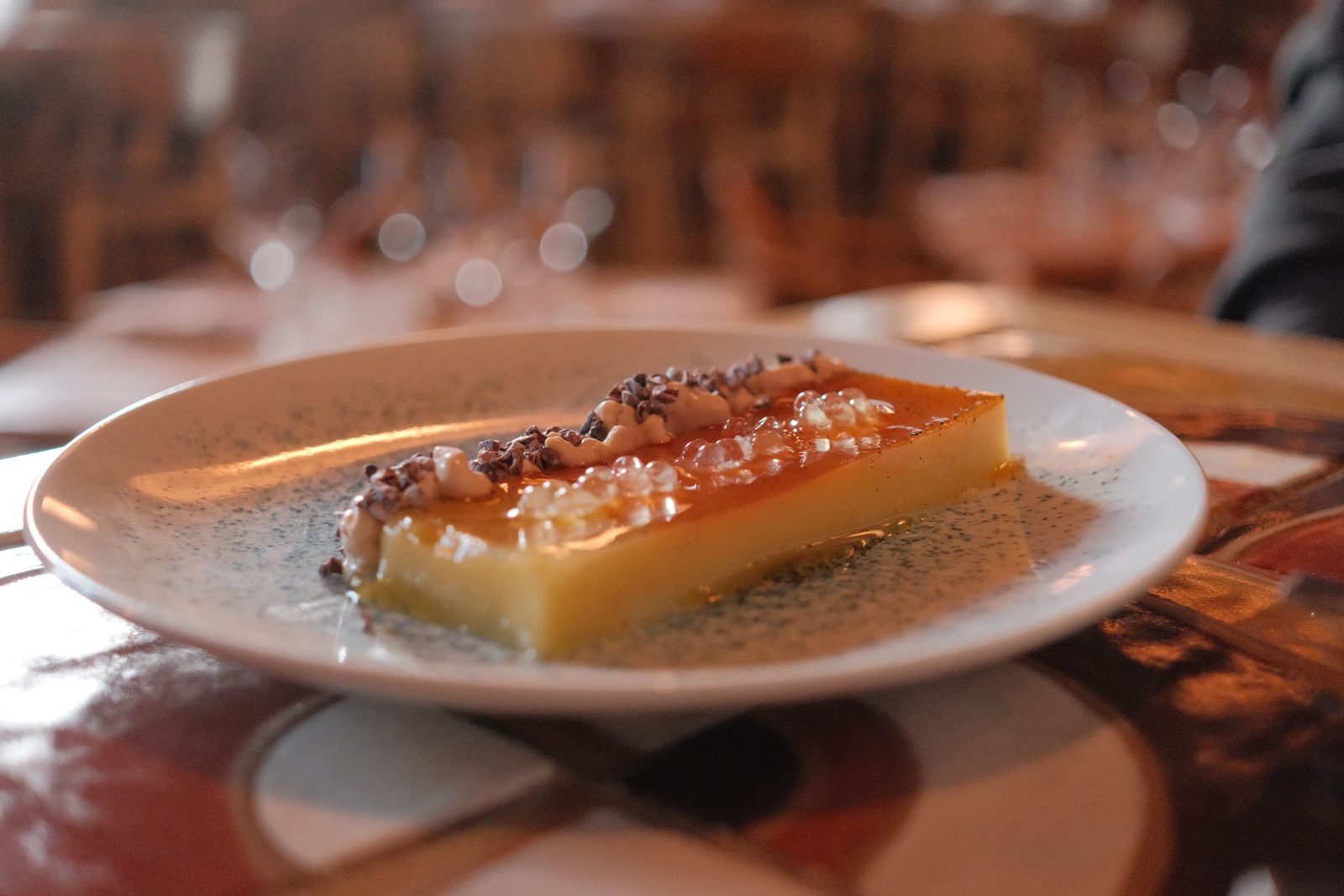 A slice of caramel flan on a speckled plate