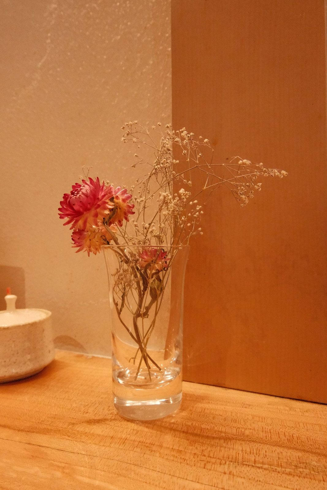 A few dried flowers in a glass on a wooden ledge