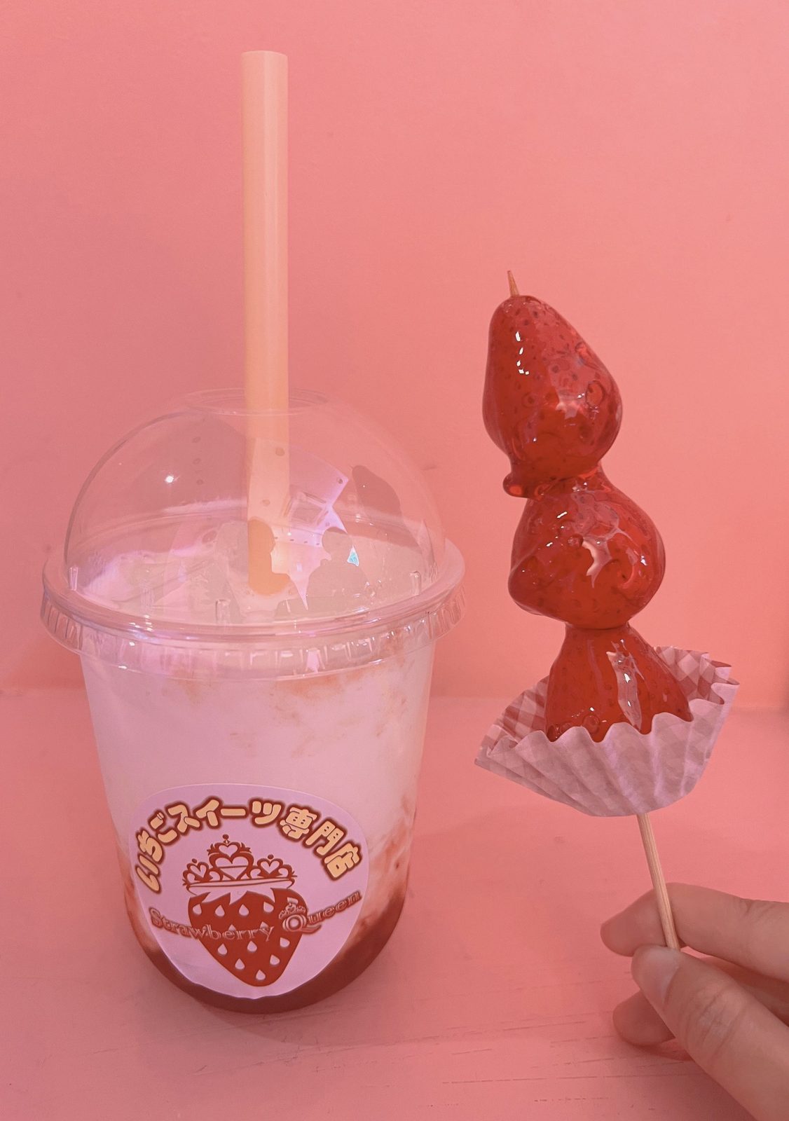 A strawberry milk drink and a candied strawberry skewer, all in pink