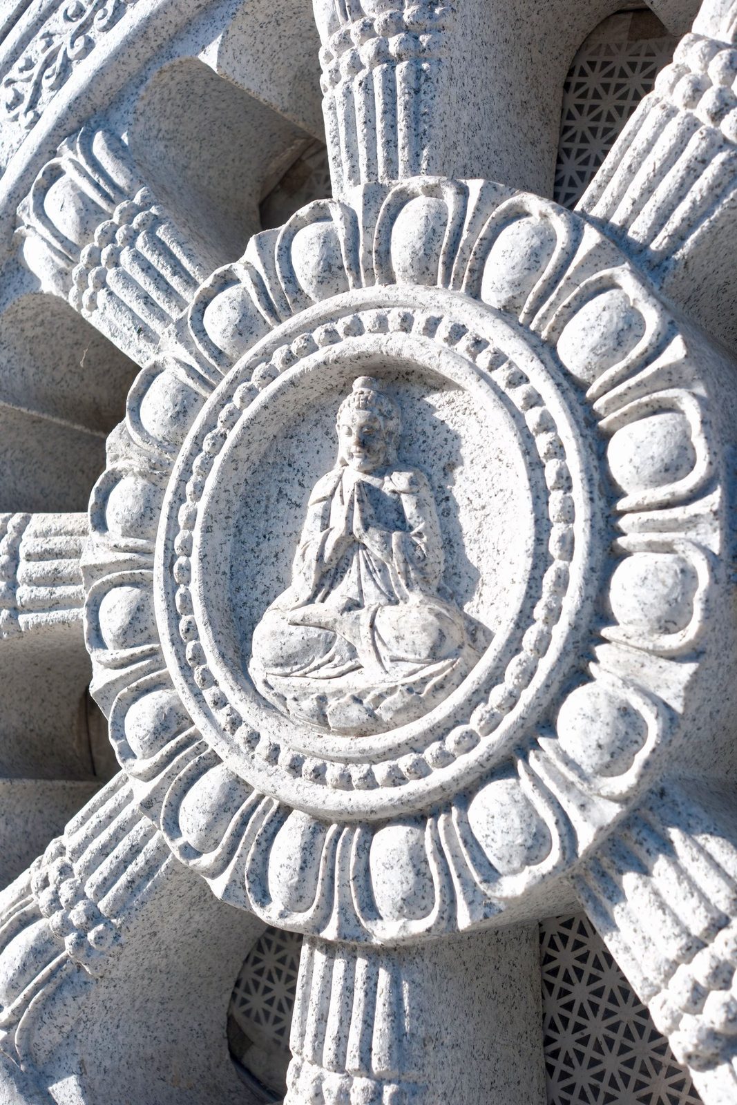 A carved stone Buddha seated at the center of a dharma wheel