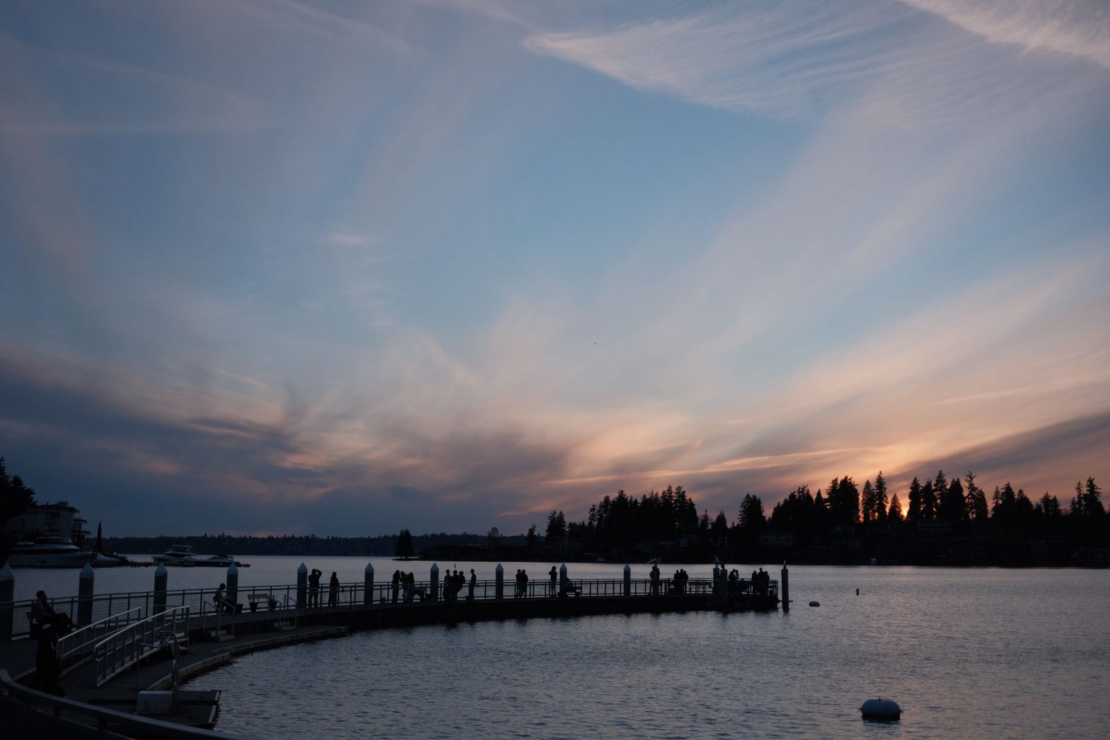 People gathered on a curved pier as the sun sets over the lake