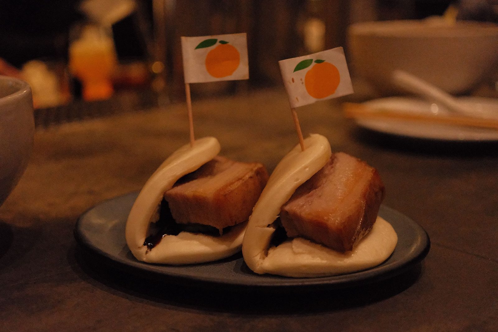 Two pork belly bao buns pinned with little orange flag picks