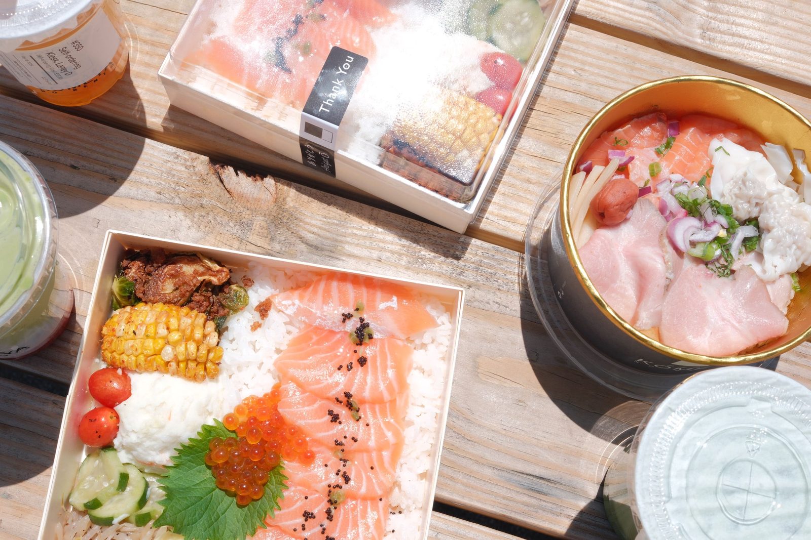 Salmon rice bowls and drinks laid out on a sunny wooden table