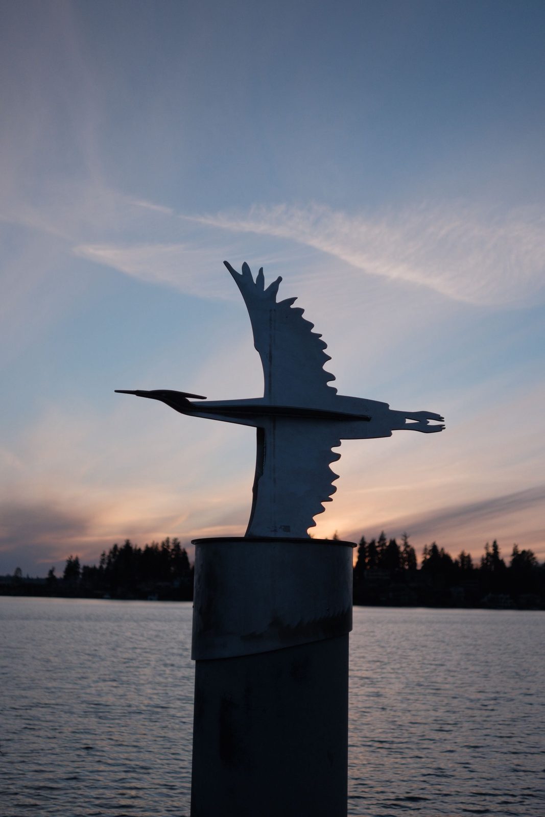 A heron sculpture silhouetted against the sunset over the water