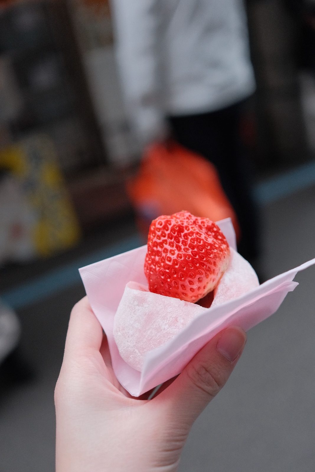 A hand holding a strawberry daifuku wrapped in pink paper