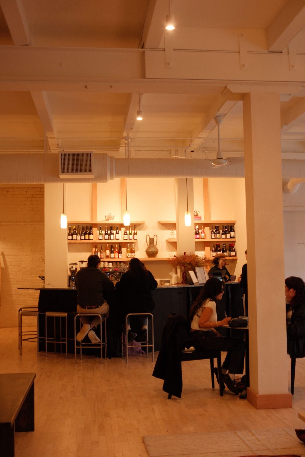 A loft cafe with wine bottles on the shelves and guests at the counter