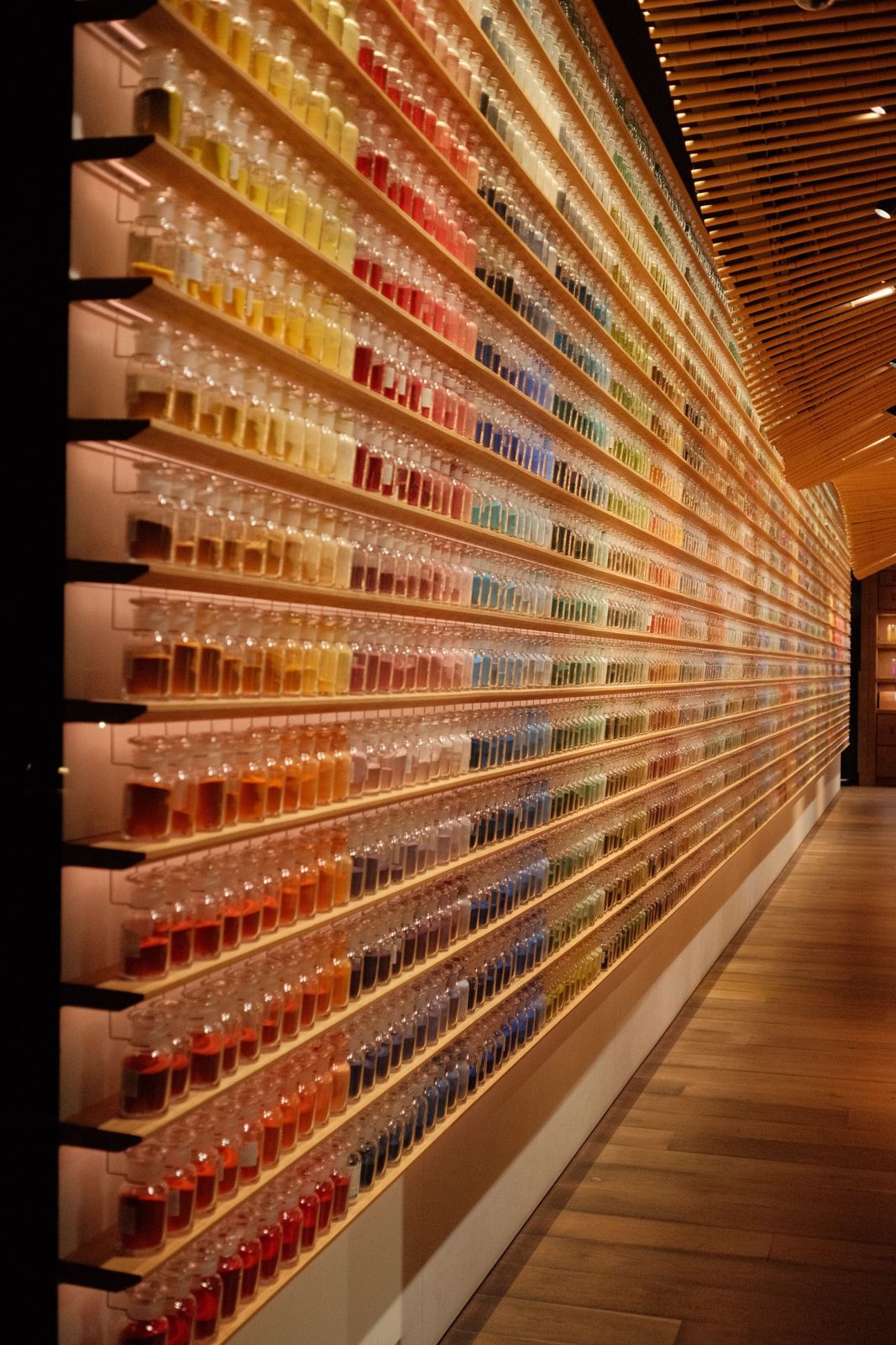 A glowing wall of colour-sorted sample bottles along a wooden corridor
