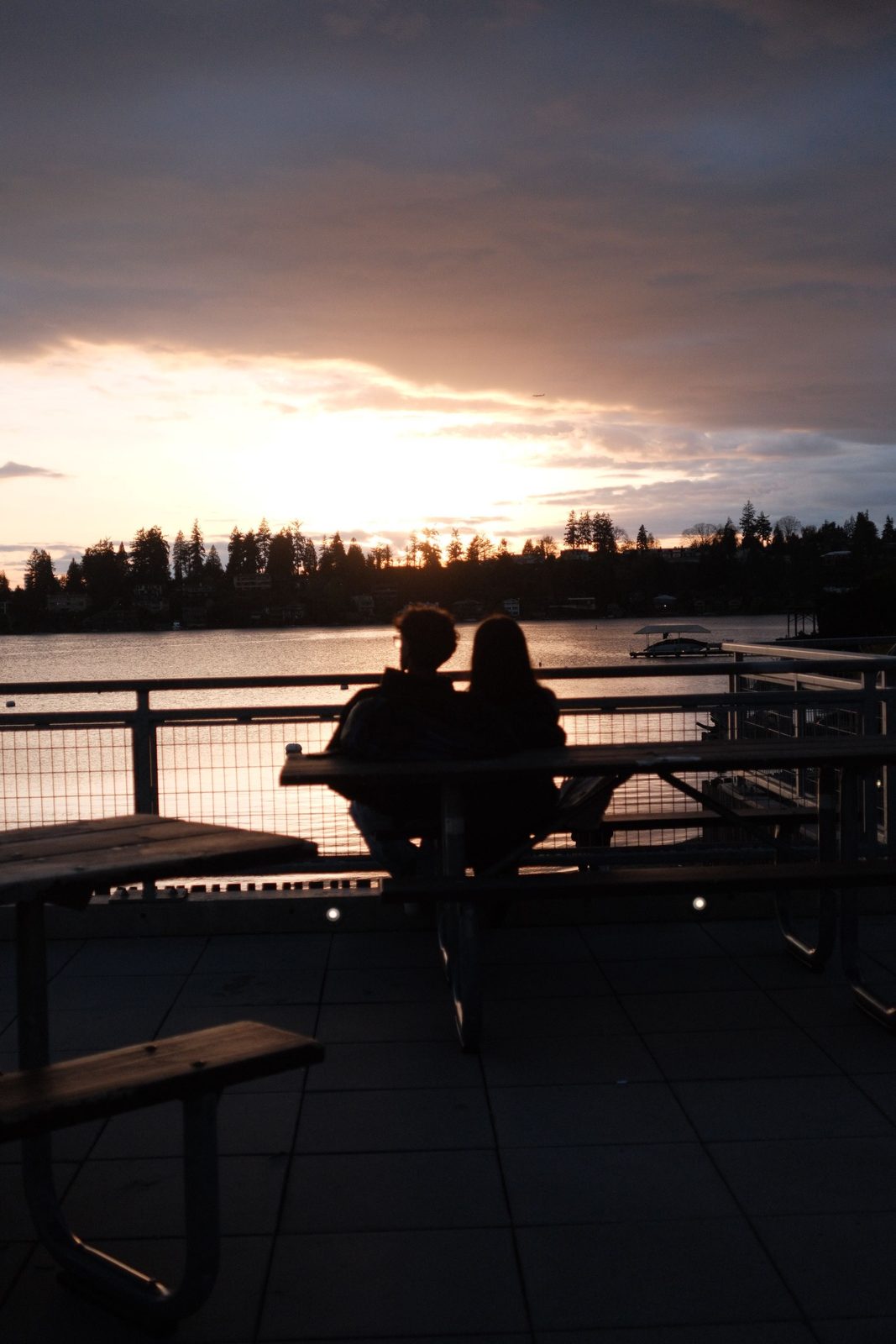 A couple silhouetted on a bench watching the sunset over the lake