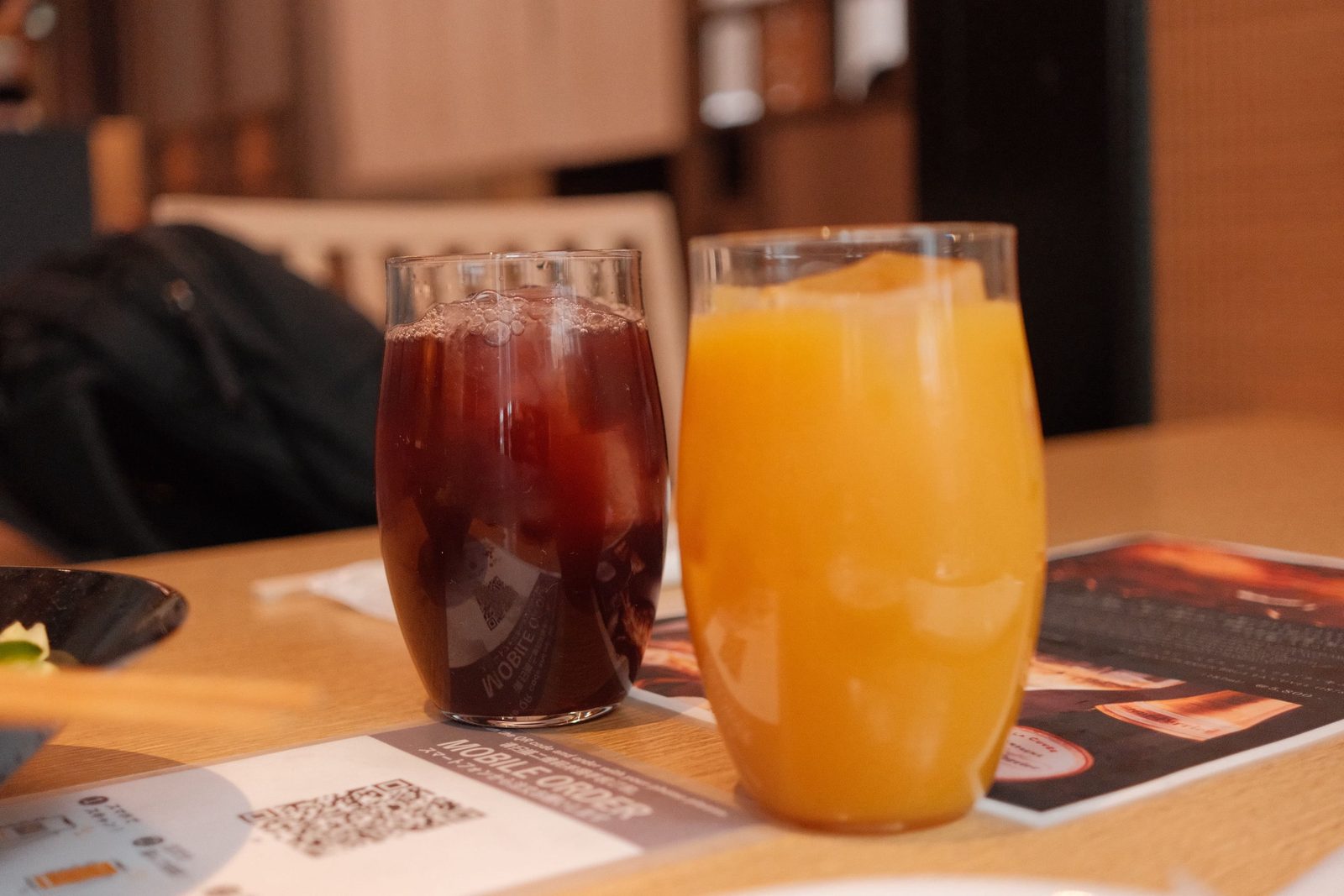 Two iced drinks, cola and orange juice, on a wooden table
