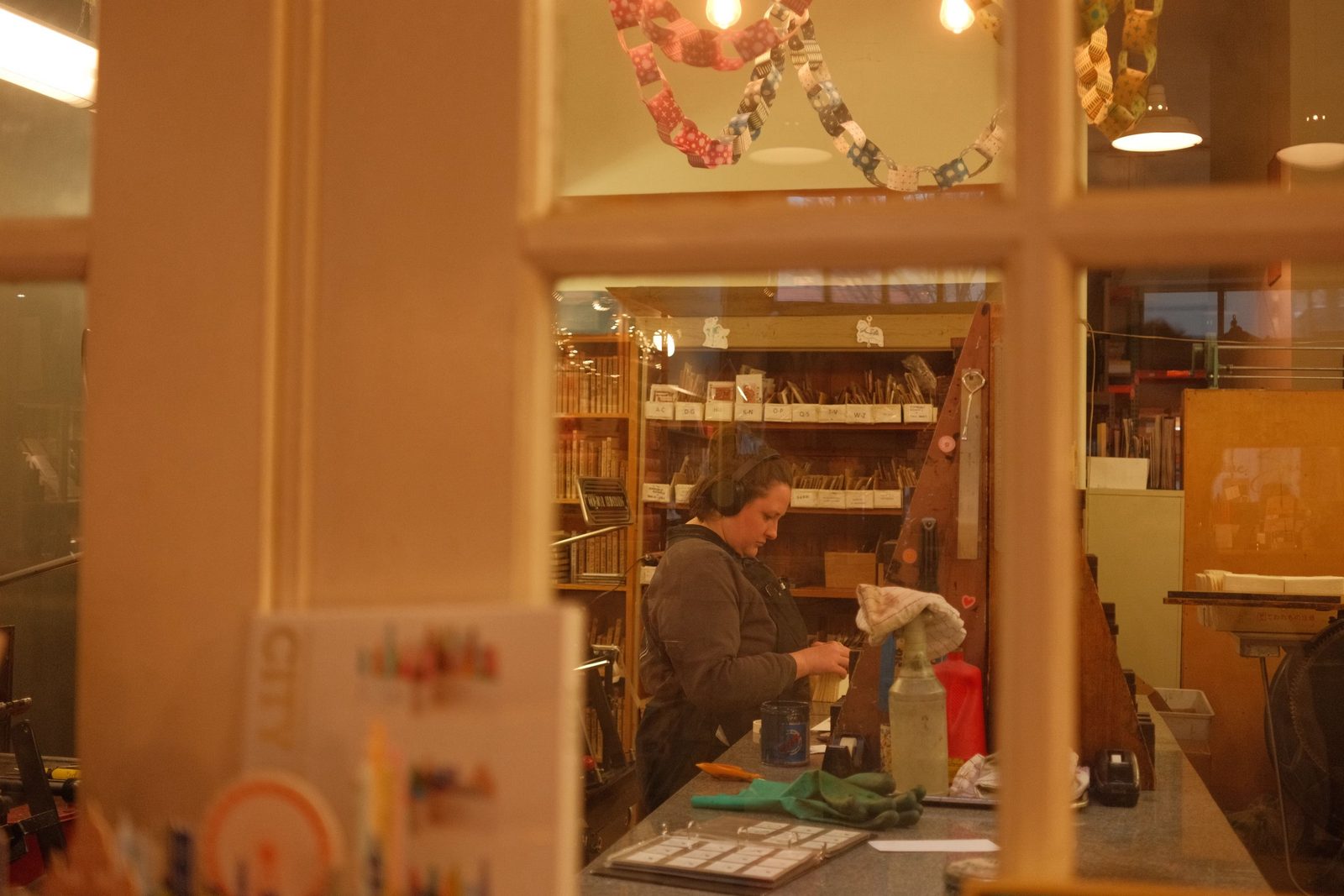 A craftsperson at work in a bindery, seen through a paned window