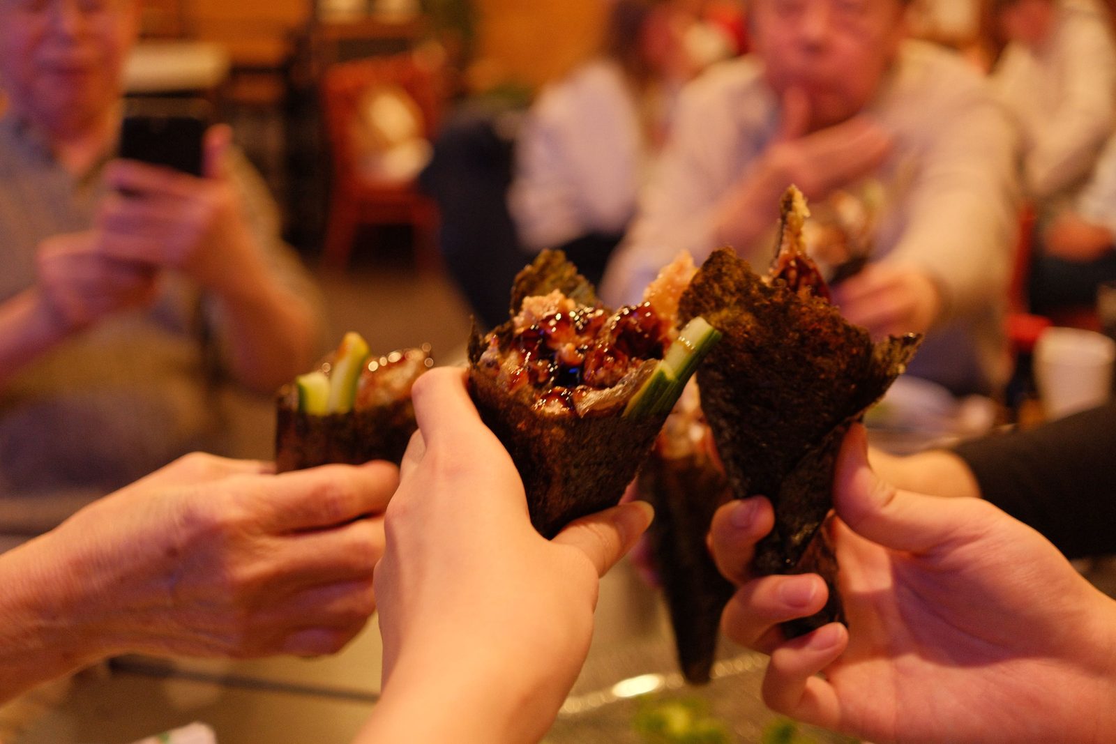 Hands clinking together over temaki hand rolls at a dinner table
