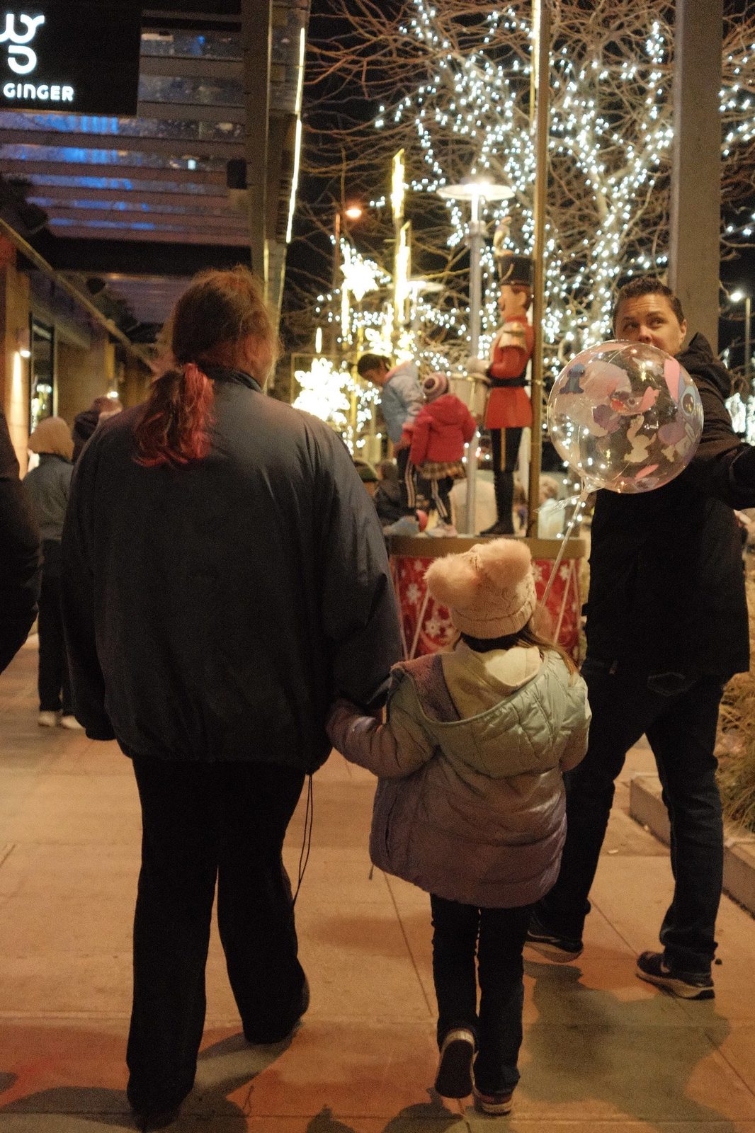 A family walking past glittering holiday lights and a nutcracker at night
