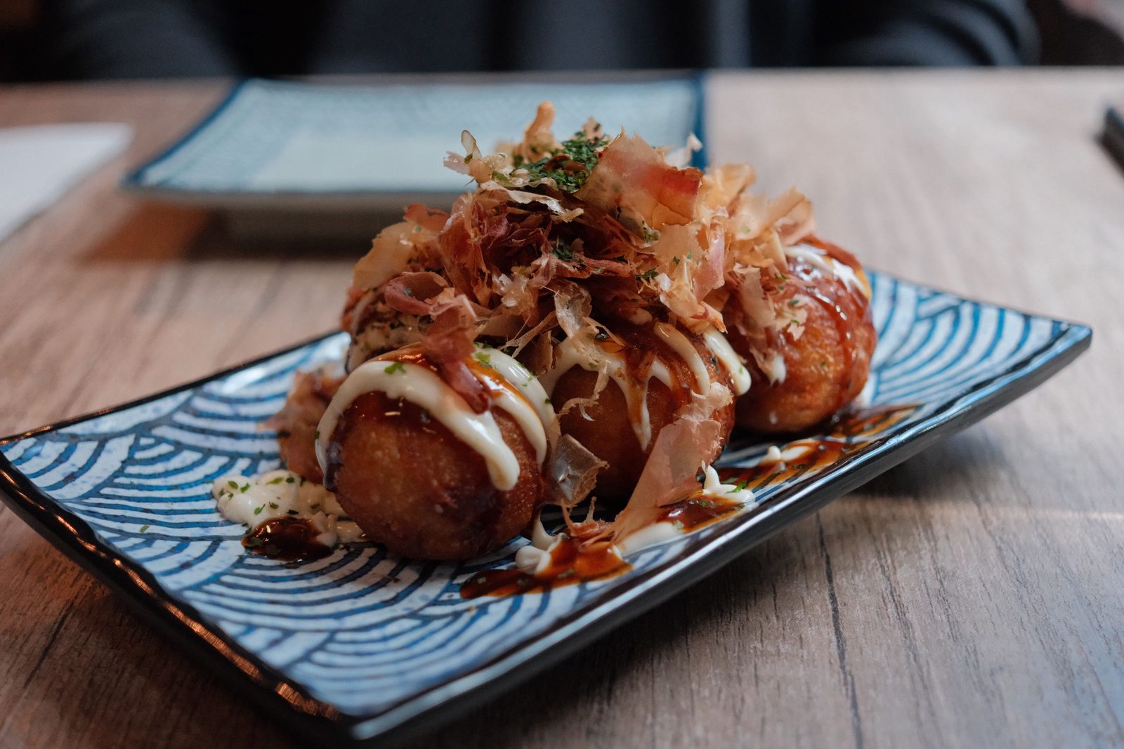 Takoyaki drizzled with mayo and bonito flakes on a blue wave plate
