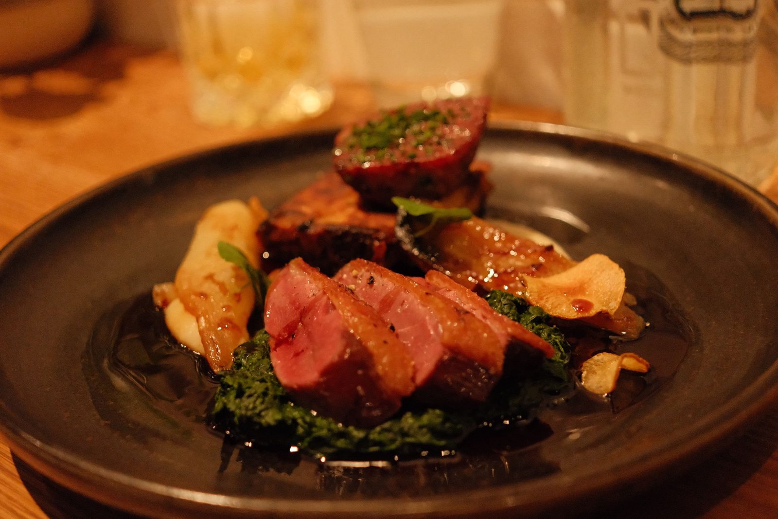 Slices of seared duck breast over greens and puree on a dark plate