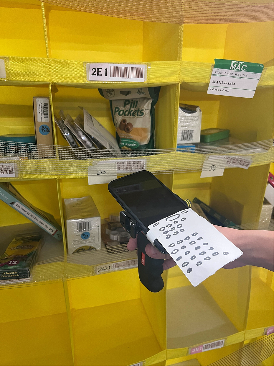 iPhone attached to a hand scanner handle with a paper keypad, held up to a warehouse bin